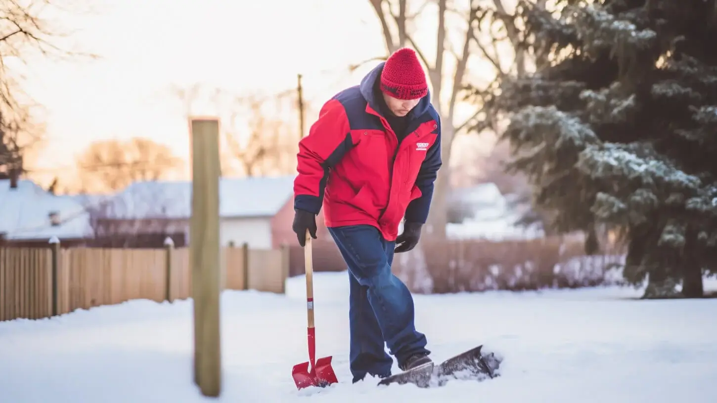 20230612_005.jpg A person in a red coat and hat shovels snow in a backyard on a winter day, working to keep the driveway ice free.
