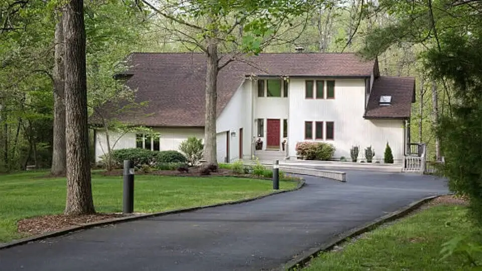 Modern two-story house with a sloped roof, surrounded by trees and a long, curved driveway enhanced by professional sealcoating for driveways.