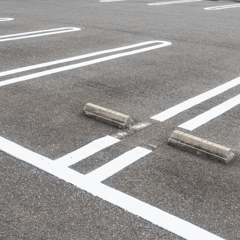 Empty parking lot with clearly marked white lines and two concrete wheel stops, showcasing pristine asphalt paving by PA's top contractors.