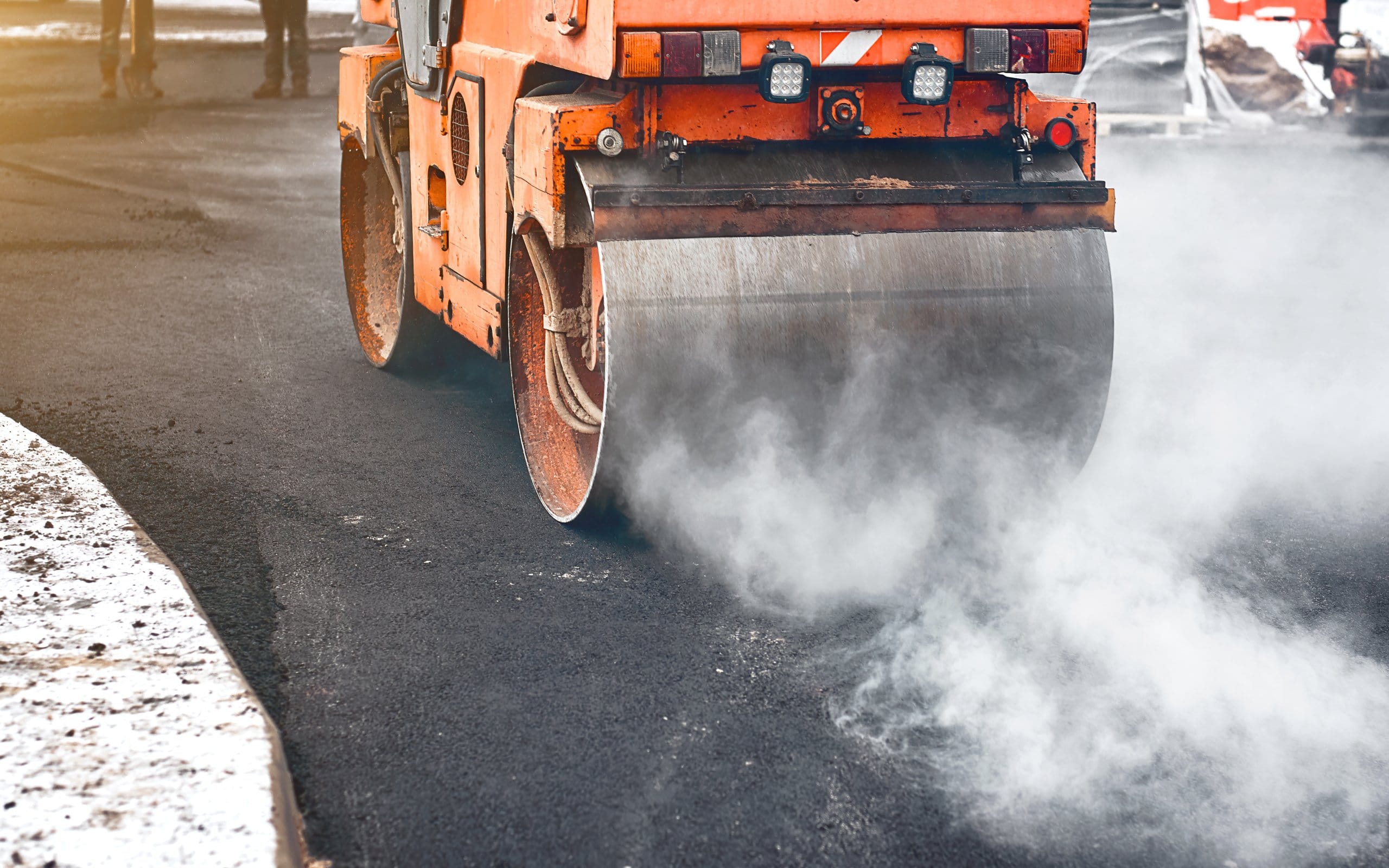Vibration roller compactor lay new asphalt surface in wintertime. Road construction, asphalt roller press hot asphalt. Asphalt paving, steamroller machine Asphalt Paving in Winter An orange steamroller methodically smooths new asphalt, with steam rising into the chilly air, showcasing the careful process of asphalt paving in winter.