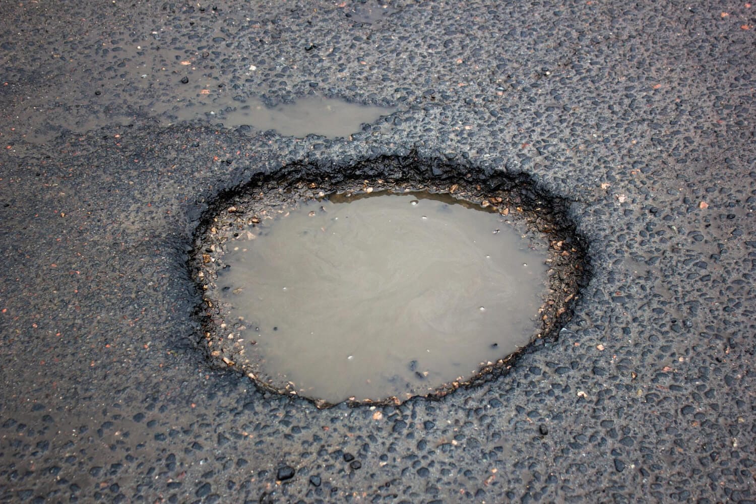 2978 A large pothole filled with murky water in the middle of an asphalt road.