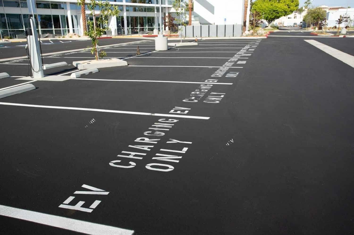 Empty parking lot with spaces marked "EV CHARGING ONLY" in white paint on the asphalt.