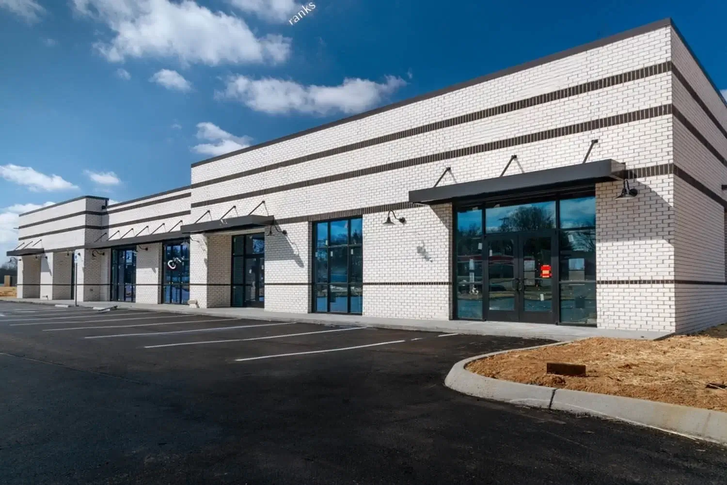 A modern, empty strip mall with white brick exterior, large glass windows, and an empty parking lot.