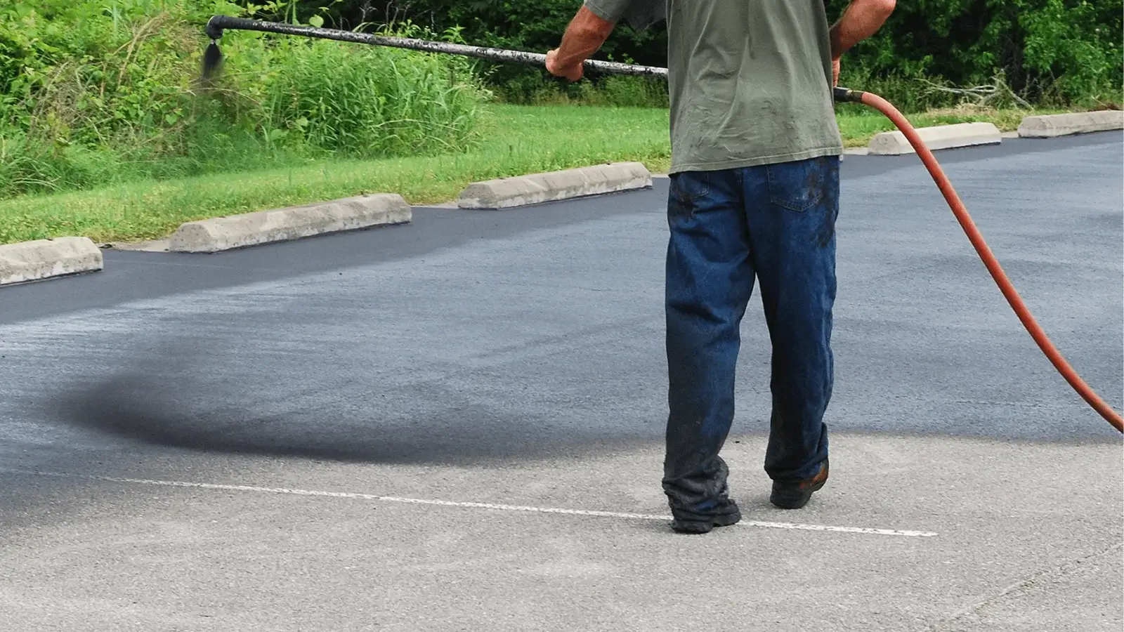 Person sealing asphalt in a parking lot with a hose, freshly coated blacktop visible.