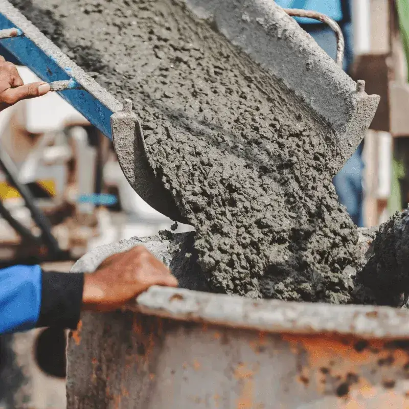 concrete-3 Wet concrete being poured from a chute into a container at a construction site, with hands guiding the process.