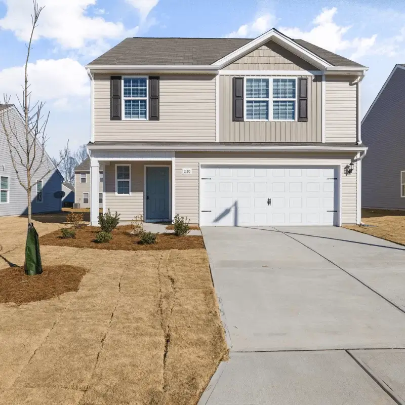 driveway-2 Two-story beige house with white garage door, driveway, and a small tree in the front yard.