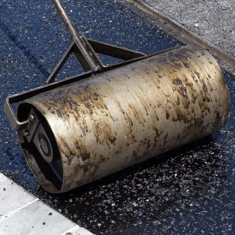 Close-up of a metal asphalt roller smoothing freshly laid black asphalt on a road surface.