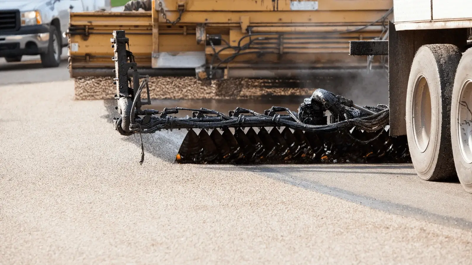 Untitled-design-24 A truck applies hot tar or asphalt to a road during a resurfacing or road repair process.